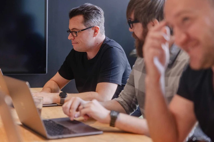 Two men looking at laptops sat down.