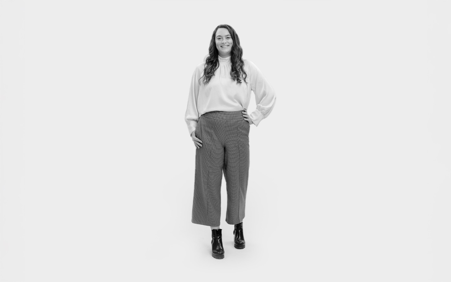 Woman stood wearing white top, grey trousers and boots.