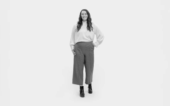 Woman stood wearing white top, grey trousers and boots.